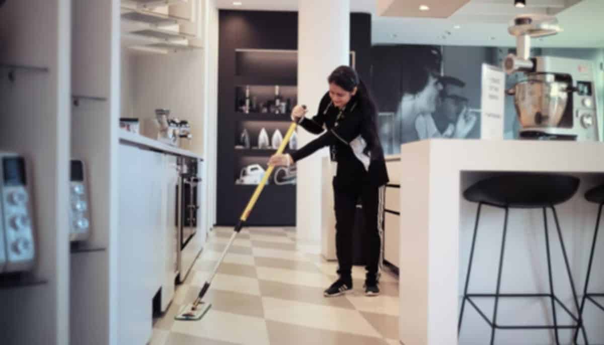 A woman cleans a tile floor with a flat mop.
